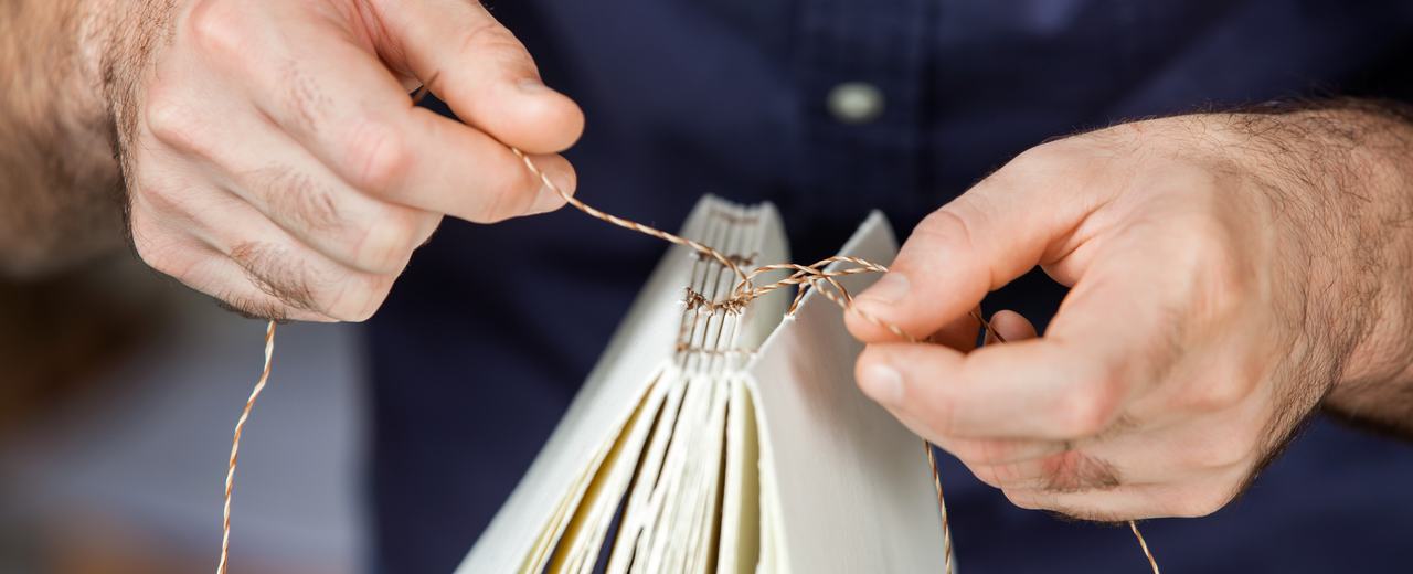 Mensch bindet mehrere Seiten zu einem Buch zusammen